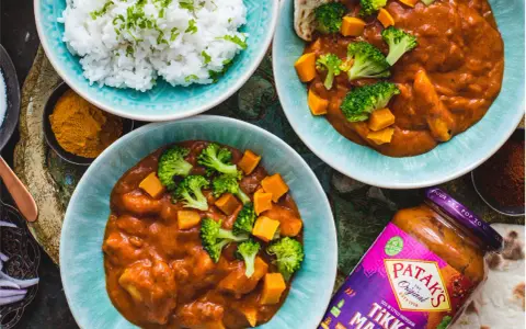 Dwa talerze z sosem Tikka Masala, ryżem, brokułami i dynią, obok słoik sosu.