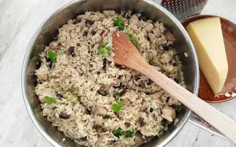 Kremowe risotto z pieczarkami i kurczakiem w garnku, obok kawałek parmezanu i tarka.