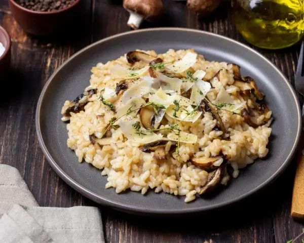 Kremowe risotto z pieczarkami, posypane parmezanem i ziołami, na ciemnym talerzu.
