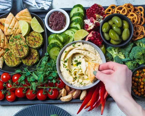 Taca z przekąskami na ognisko: hummus, falafel, warzywa, owoce, pieczywo i paluszki.