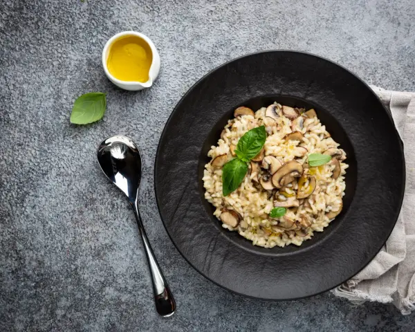 Kremowe risotto z grzybami na czarnym talerzu, obok łyżka i oliwa.