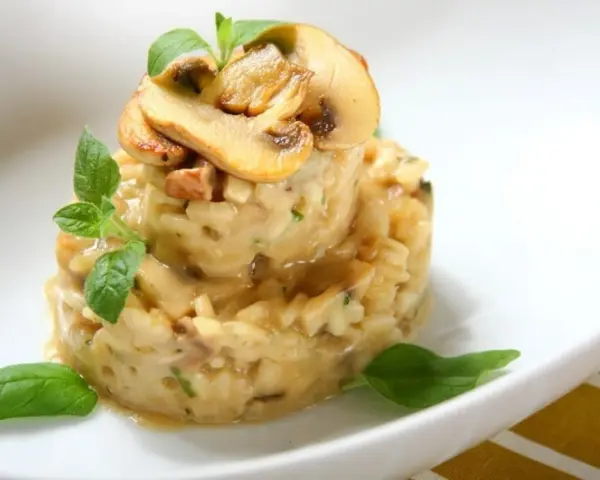 Kremowe risotto z grzybami i ziołami, udekorowane plasterkami pieczarek i listkami bazylii.
