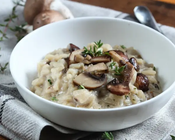 Kremowe risotto z pieczarkami i serem pleśniowym, udekorowane świeżym tymiankiem.