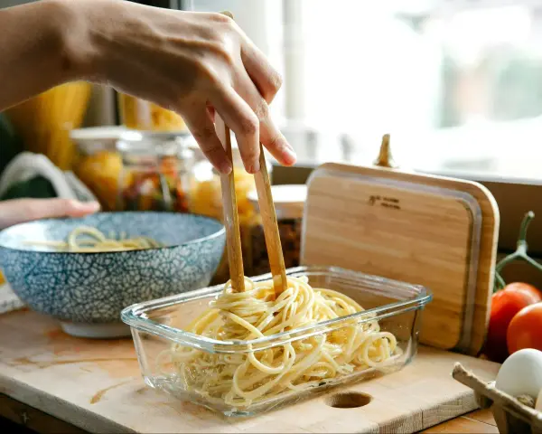 Dłoń trzymająca pałeczki wyciąga makaron spaghetti z szklanego pojemnika.