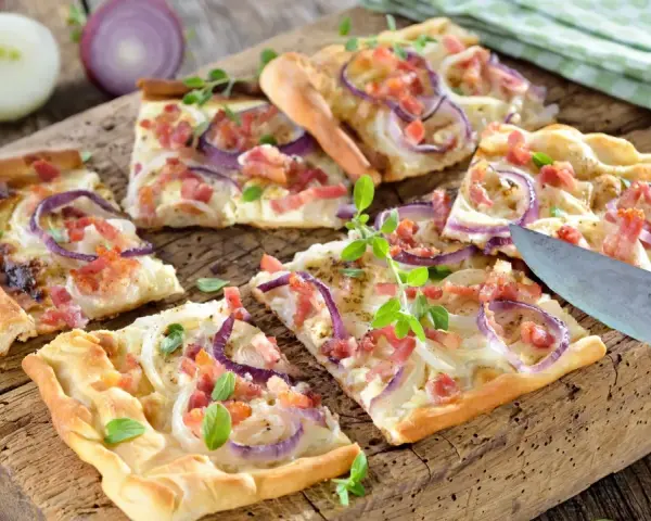 Kawałki pizzy z cebulą i boczkiem na drewnianej desce.