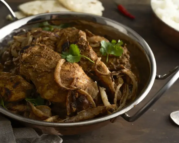 Kurczak w sosie garam masala z cebulą i kolendrą w metalowej misie.
