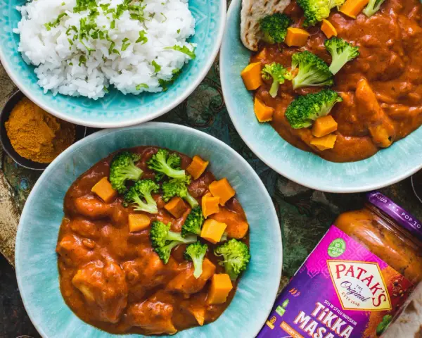 Dwa talerze z sosem Tikka Masala, ryżem, brokułami i dynią, obok słoik sosu.