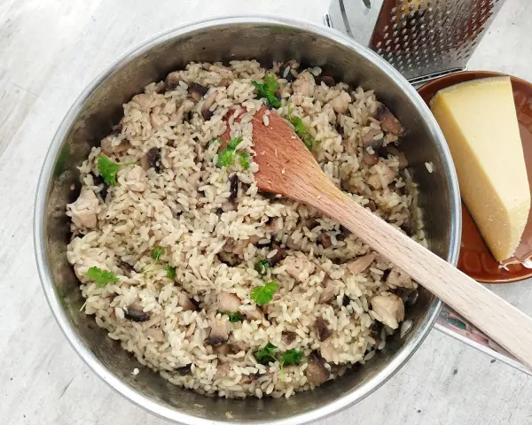 Kremowe risotto z pieczarkami i kurczakiem w garnku, obok kawałek parmezanu i tarka.