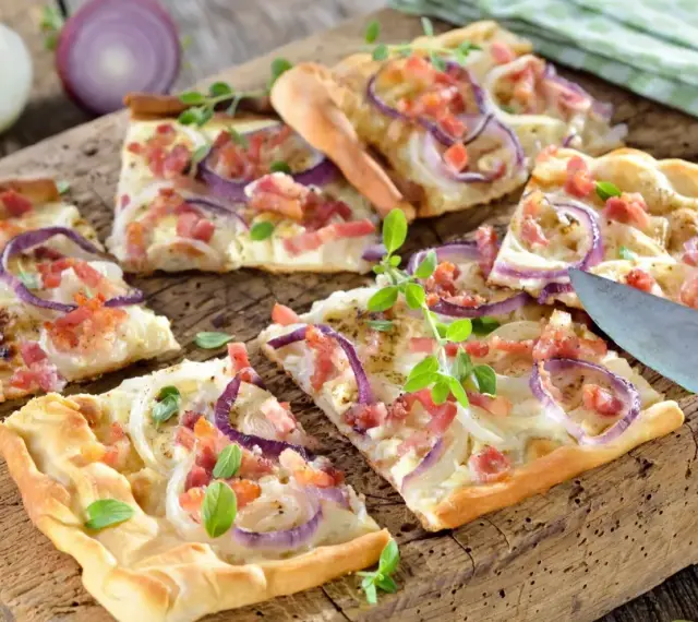 Kawałki pizzy z cebulą i boczkiem na drewnianej desce.