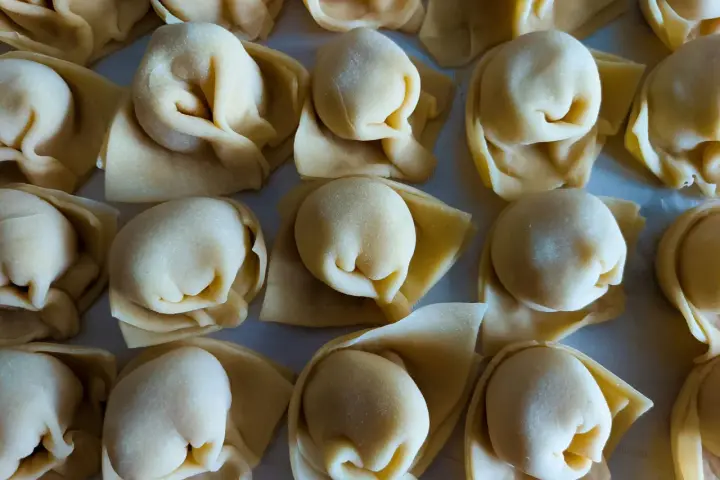Surowe tortellini ułożone rzędami na jasnym tle.