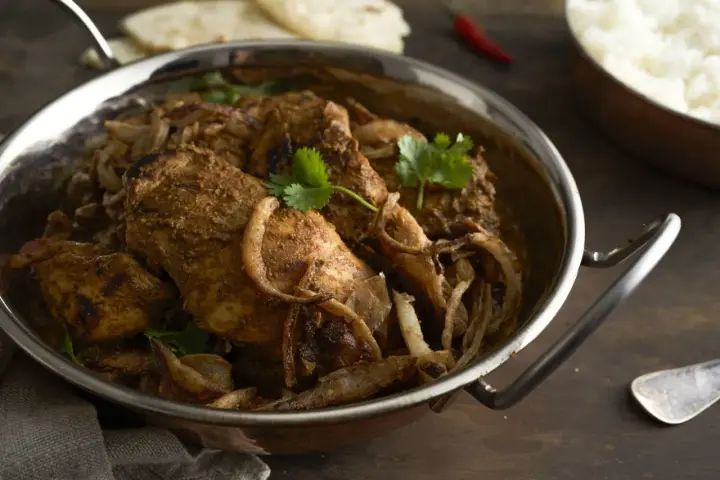 Kurczak w sosie garam masala z cebulą i kolendrą w metalowej misie.