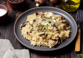 Kremowe risotto z pieczarkami, posypane parmezanem i ziołami, na ciemnym talerzu.
