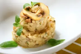 Kremowe risotto z grzybami i ziołami, udekorowane plasterkami pieczarek i listkami bazylii.