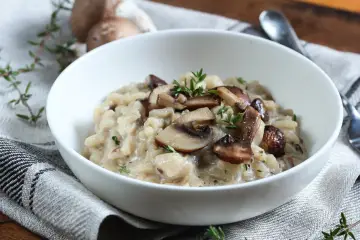 Kremowe risotto z pieczarkami i serem pleśniowym, udekorowane świeżym tymiankiem.
