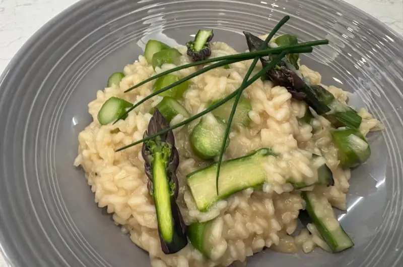 Kremowe risotto z zielonymi szparagami i szczypiorkiem na szarym talerzu.