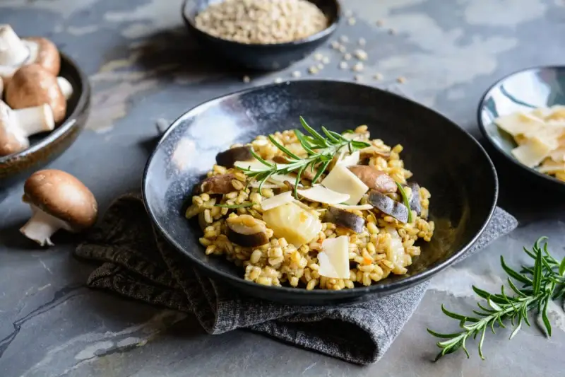 Miseczka risotto z grzybami i parmezanem, udekorowana rozmarynem.