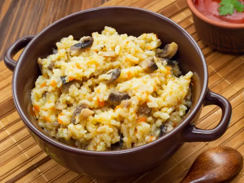 Kremowe risotto z grzybami i marchewką w brązowej misce, obok drewniana łyżka.